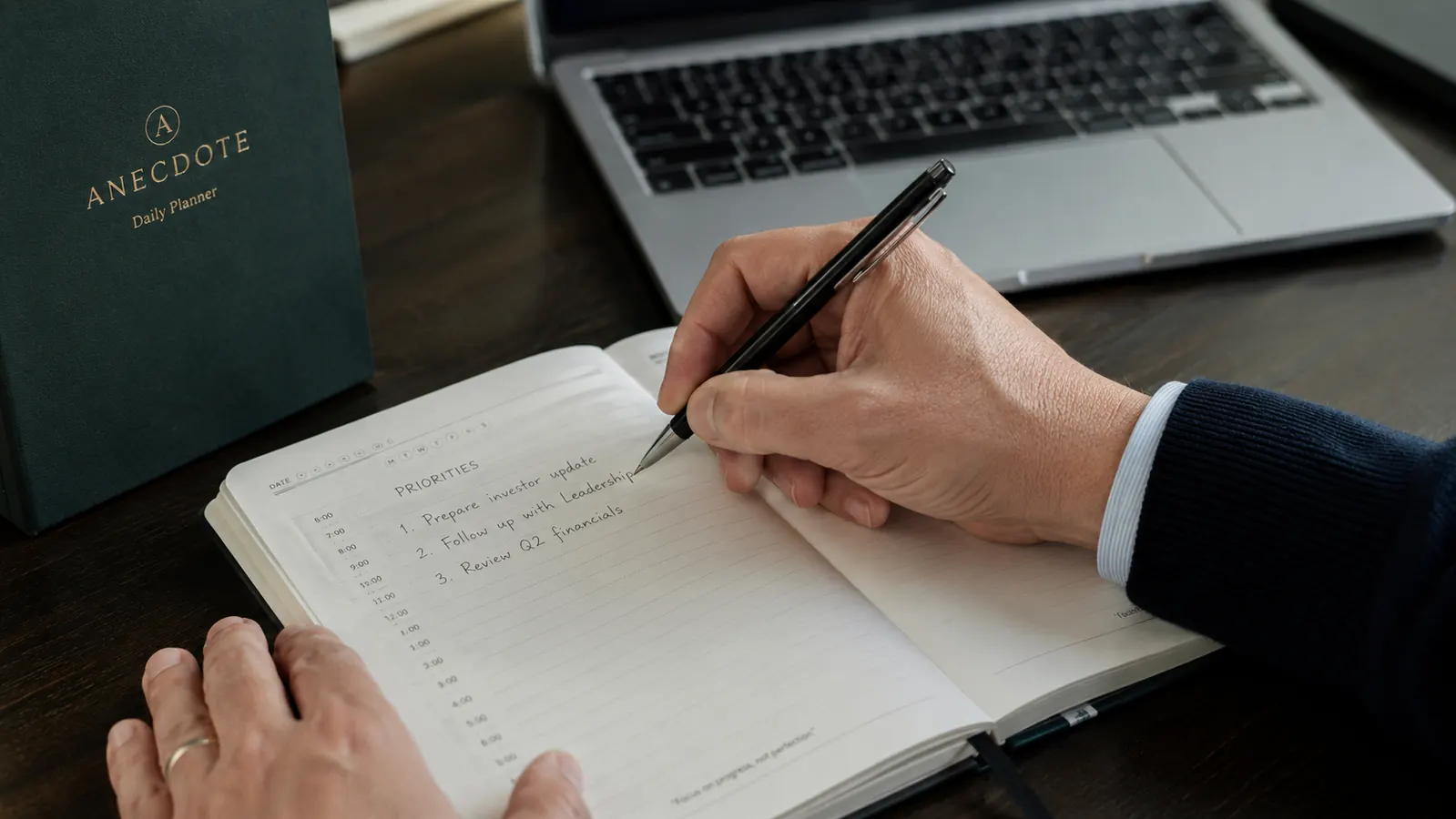 Hand writing weekly goals into the Anecdote Daily Planner, planner open to a weekly overview page