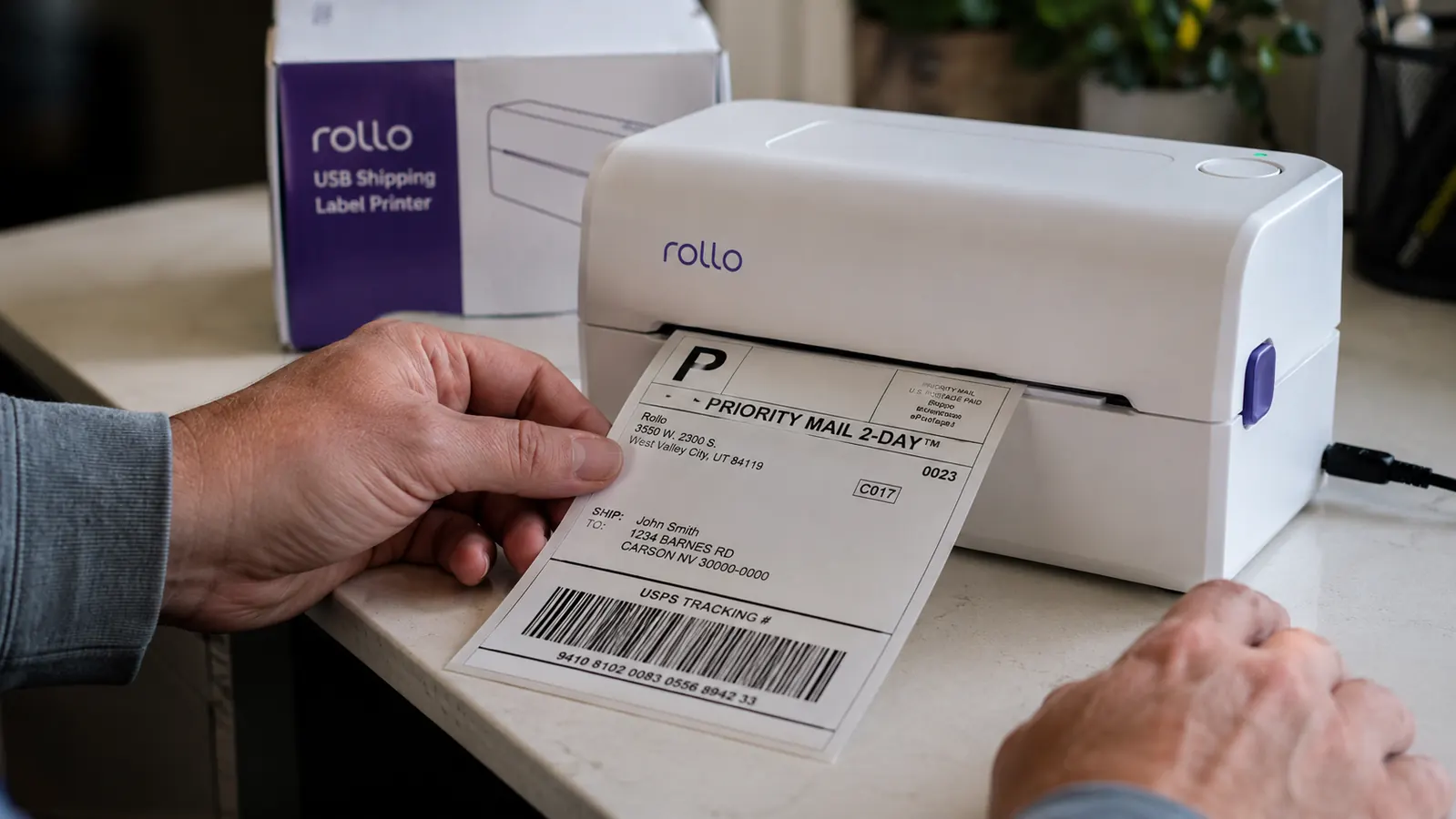 Close-up of a Rollo label printer with a fresh 4x6 shipping label printing out, USB cable visible
