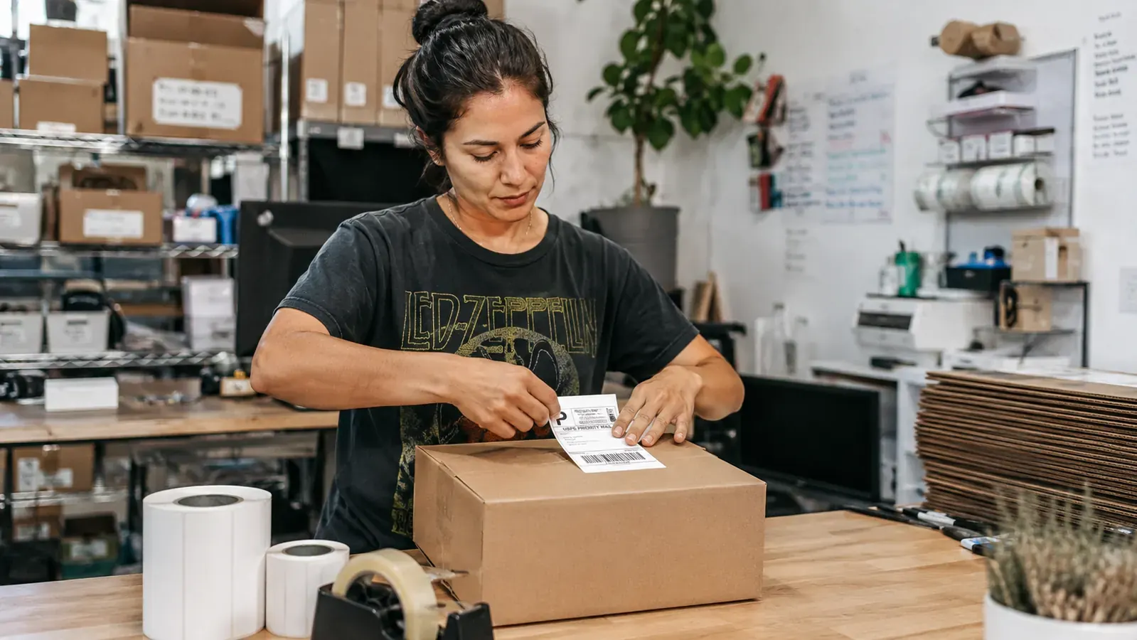 Person peeling a Rollo-printed shipping label off a roll and applying it to a cardboard shipping box
